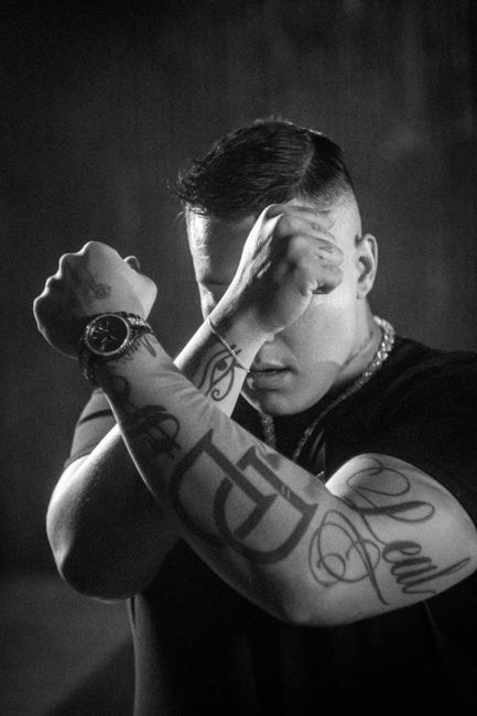 Intense black and white portrait of a tattooed person posing with crossed arms.