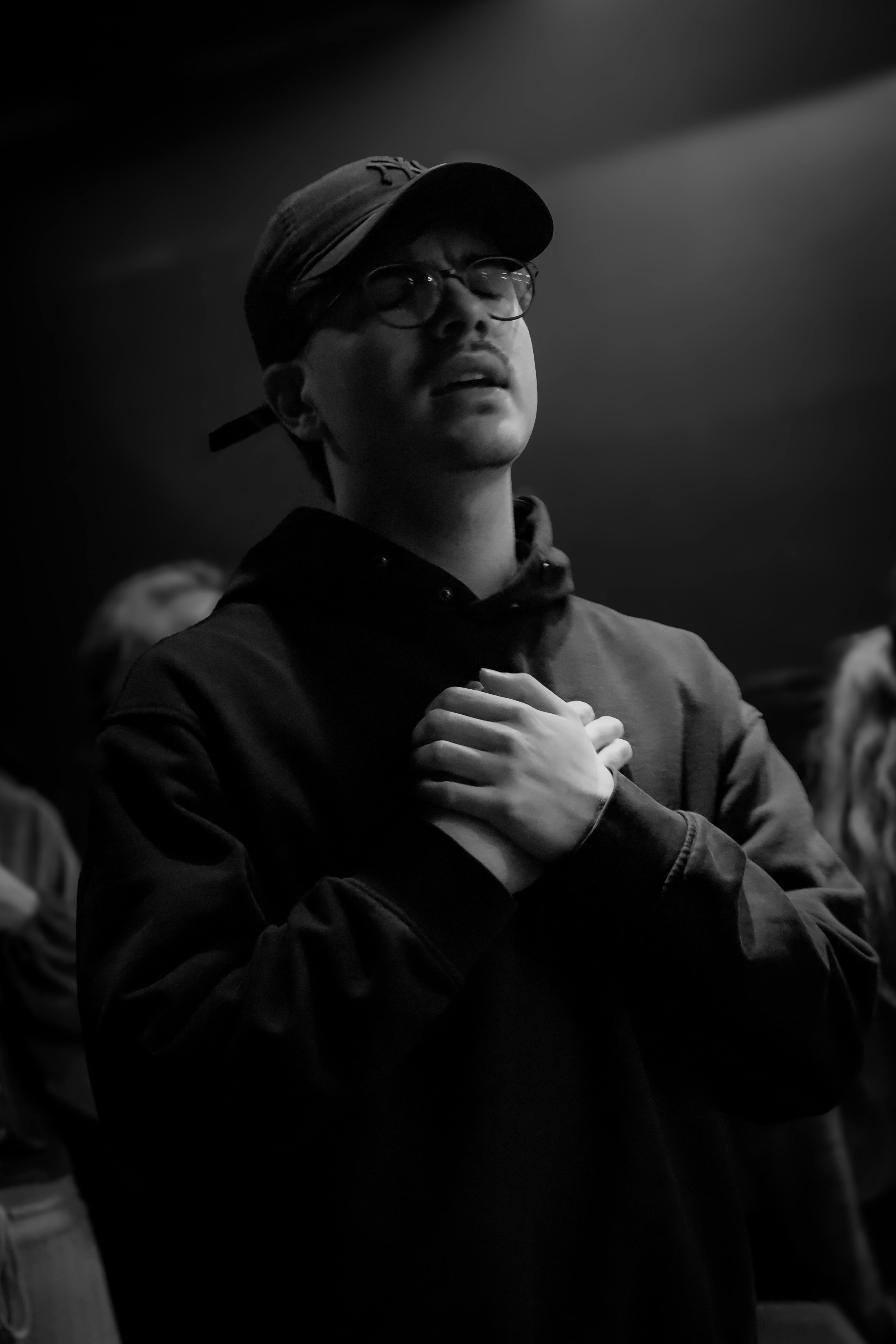 Gratuit Un bărbat contemplativ într-un cadru întunecat, ținându-și mâinile la piept. Stare de spirit emoțională și reflexivă. Fotografie de stoc