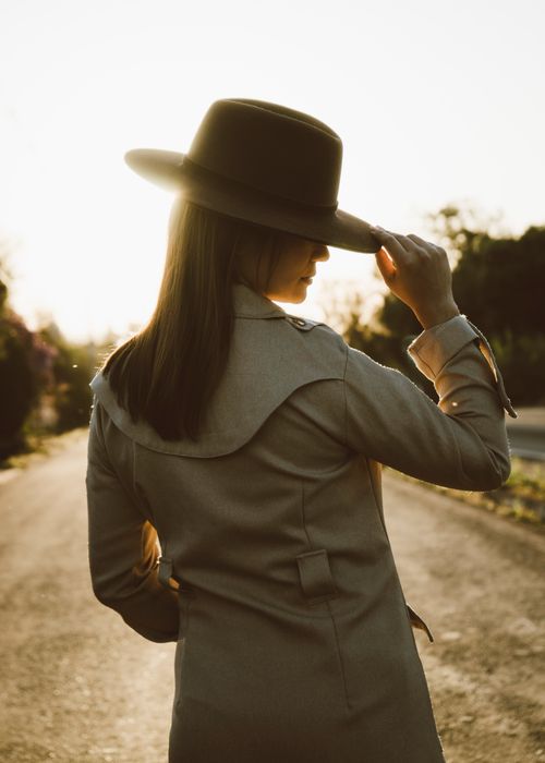 Free Back view of a woman in a hat on a sunlit road, exuding mystery and style. Stock Photo