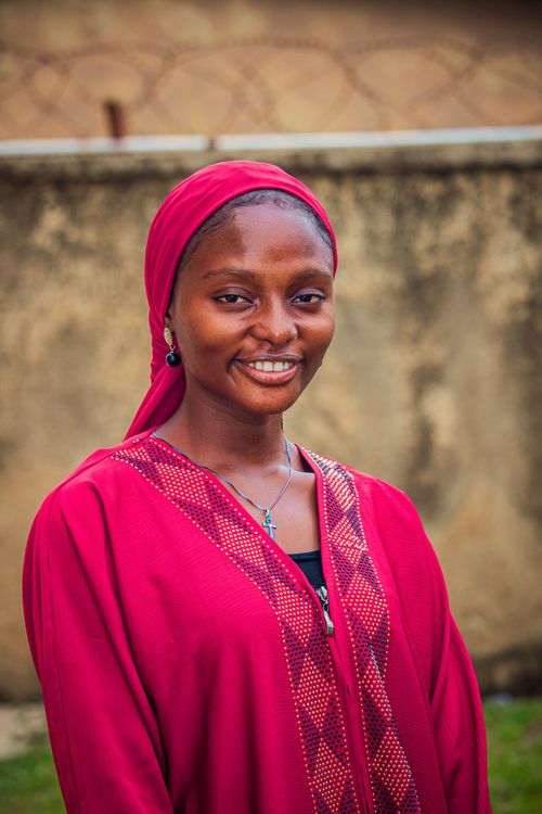 Free Portrait of a young woman wearing a red hijab, smiling against an outdoor background. Stock Photo