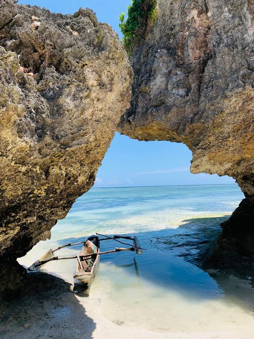 Free A traditional wooden boat docked in a serene tropical beach cove under large rock formations. Stock Photo