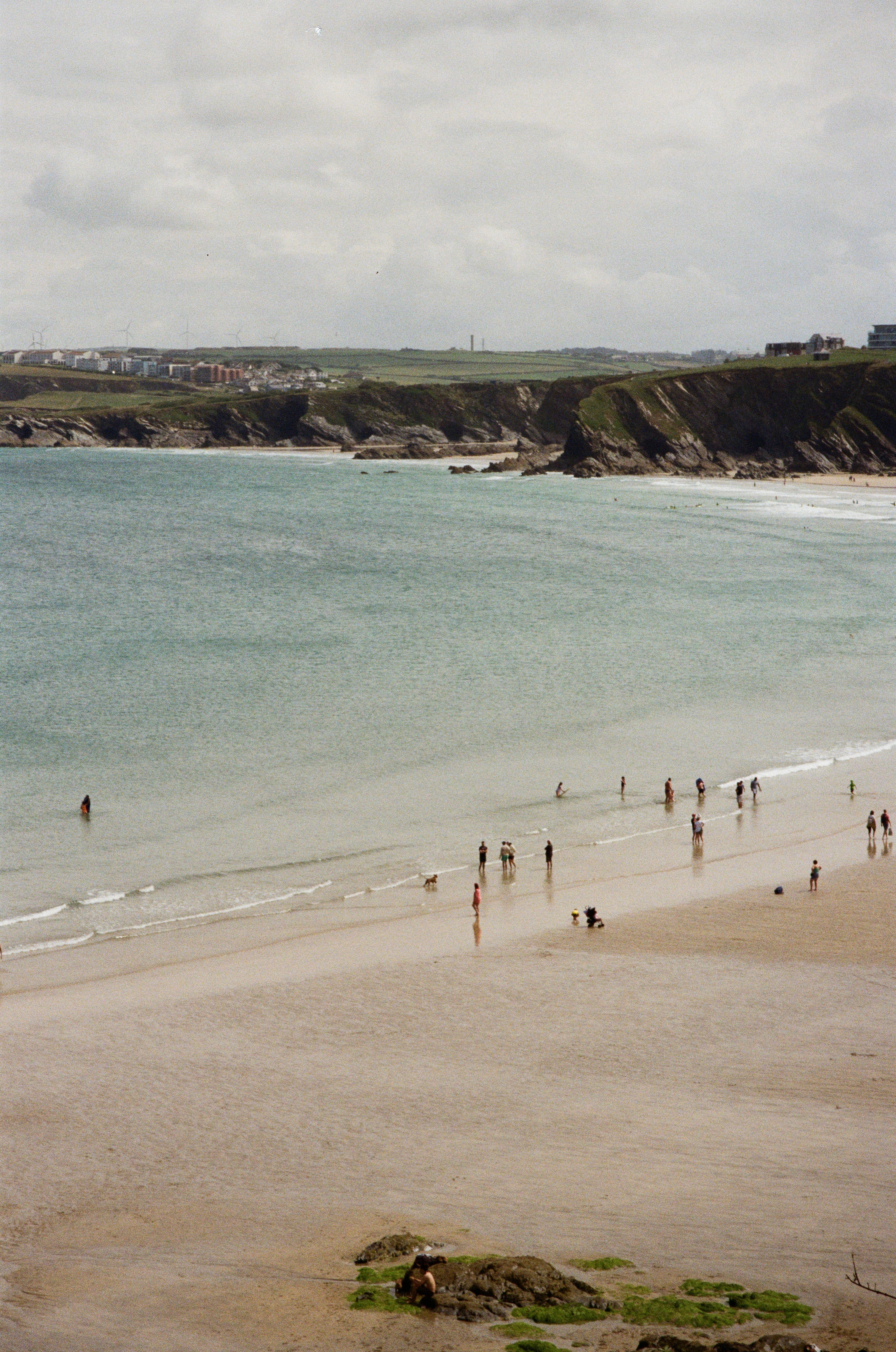 A Newquay-style bay with wind turbines on the headland and families on the sand