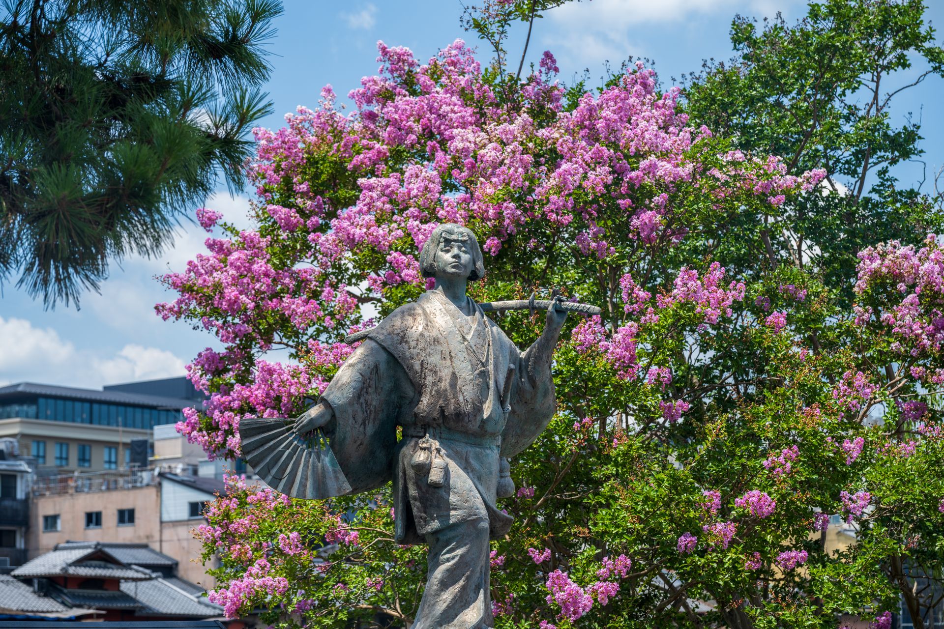 Statue of a traditional Japanese figure with vibrant pink flowers in the background.