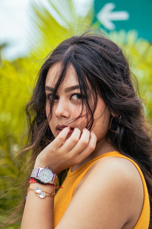 Free A captivating portrait of a woman with a thoughtful expression, standing amidst vibrant green foliage. Stock Photo