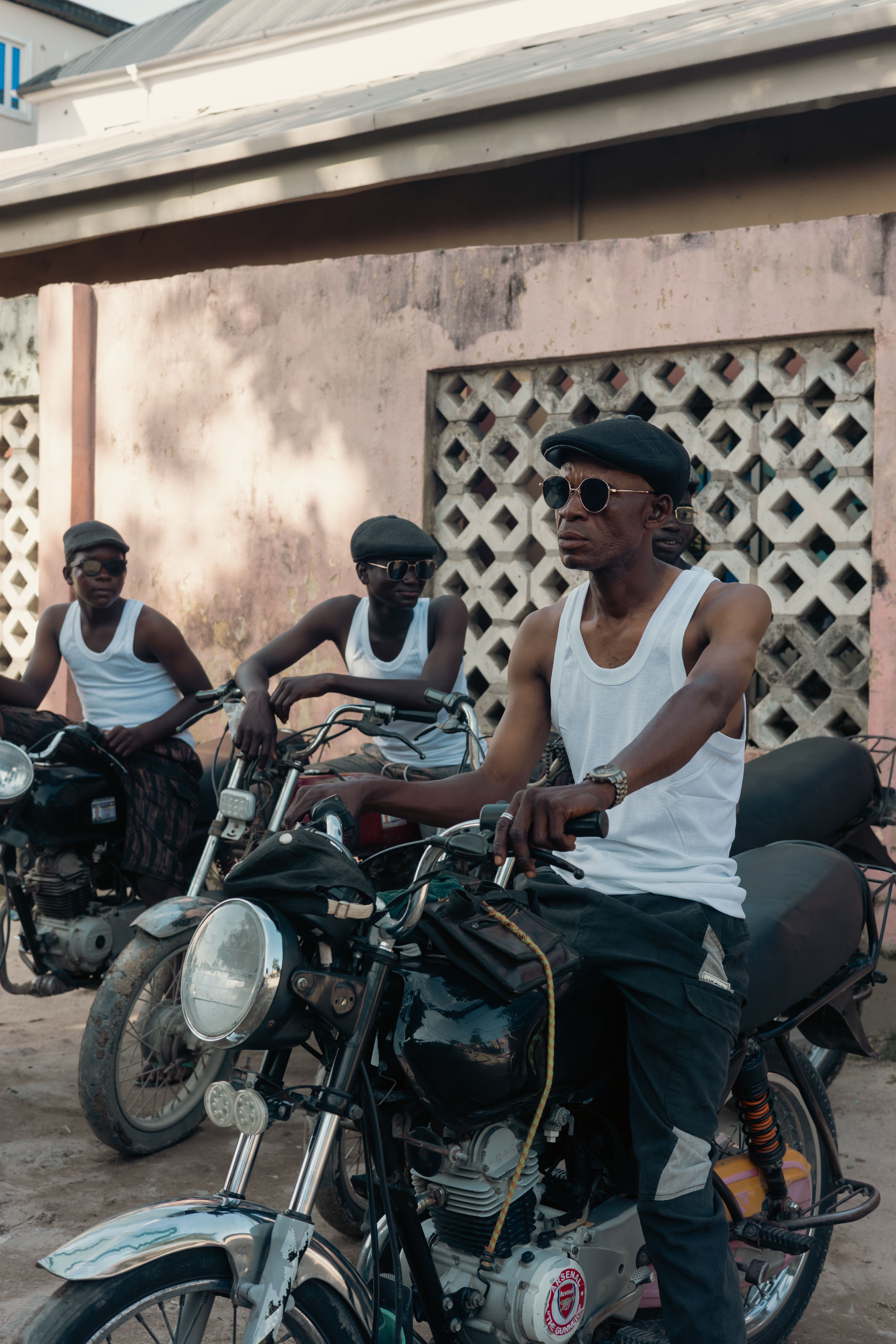 Three men on motorcycles wearing sunglasses and caps on a Lagos street.