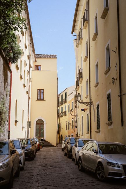Charming narrow alleyway in Italy with parked cars and tall yellow buildings.