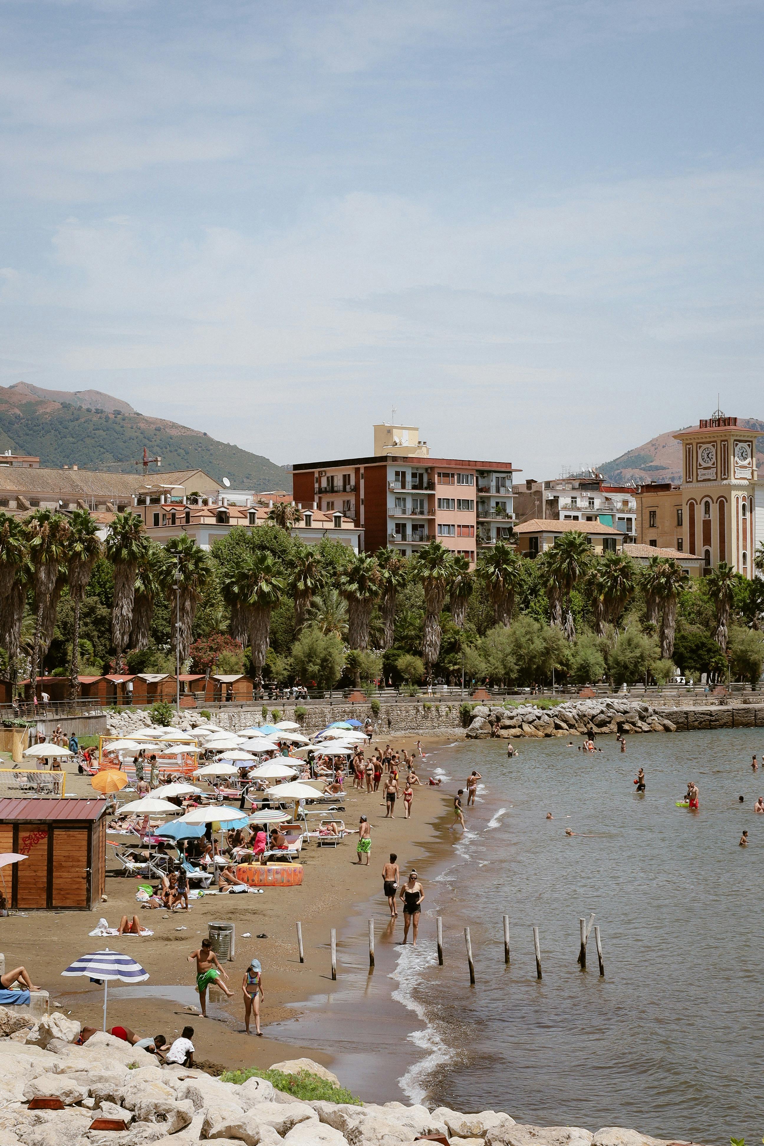Lively beachfront with umbrellas, people, and urban skyline in the background on a clear day.