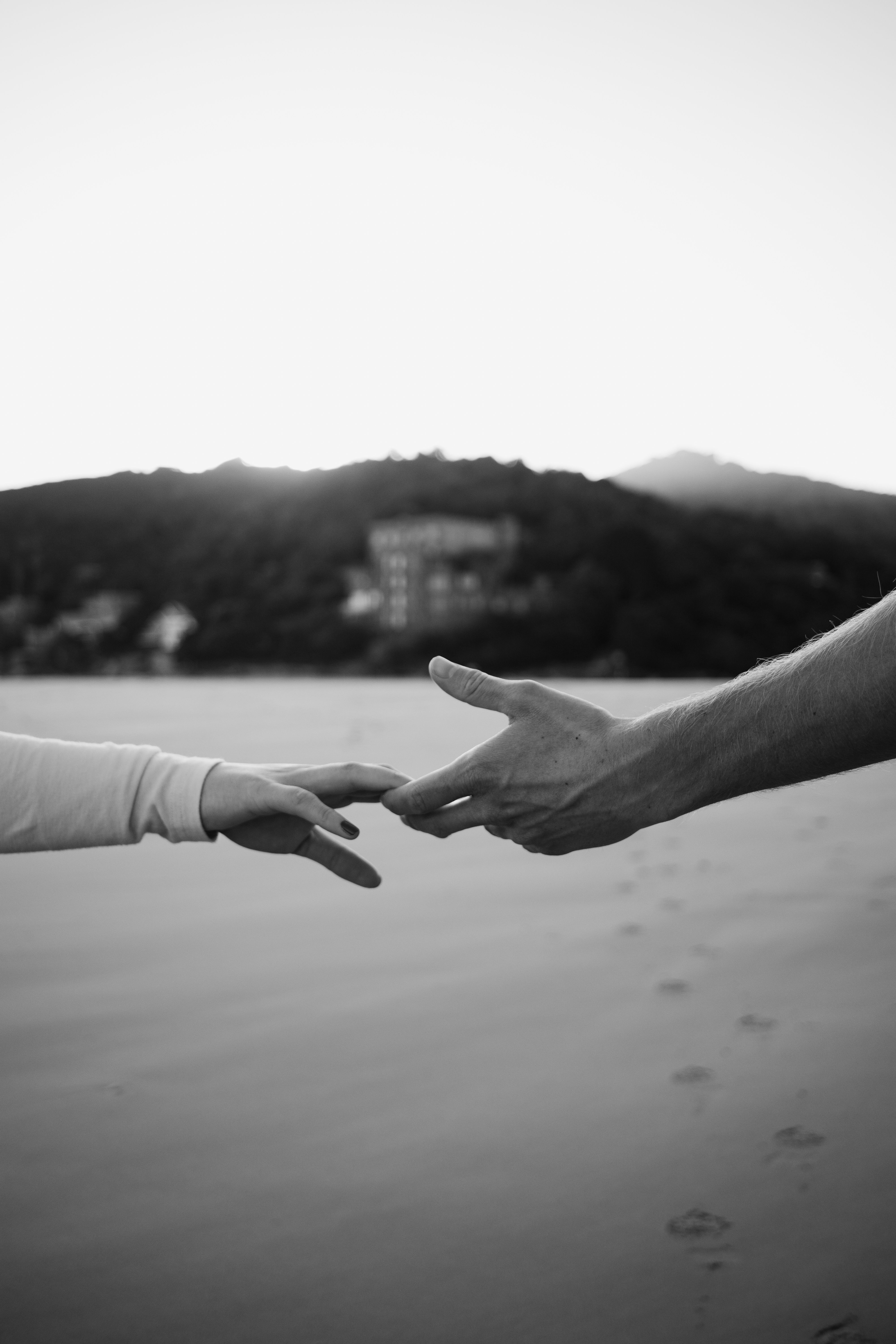 Two hands reaching out towards each other on a tranquil beach in black and white.