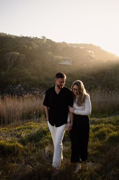 A couple walking hand in hand through a peaceful, sunlit meadow during sunset, exuding warmth and romance.