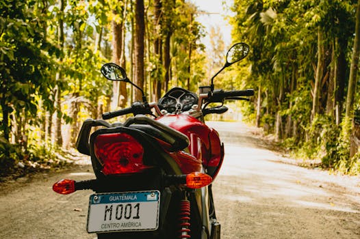 A red motorcycle parked on a tree-lined dirt road in Guatemala, capturing a scenic travel moment.