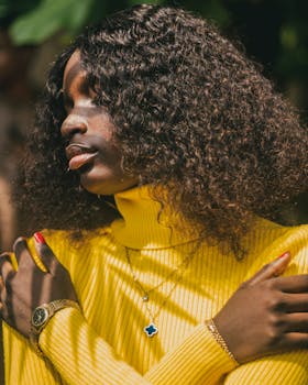 Charming outdoor portrait of a woman in a vibrant yellow sweater, bathed in warm sunlight.