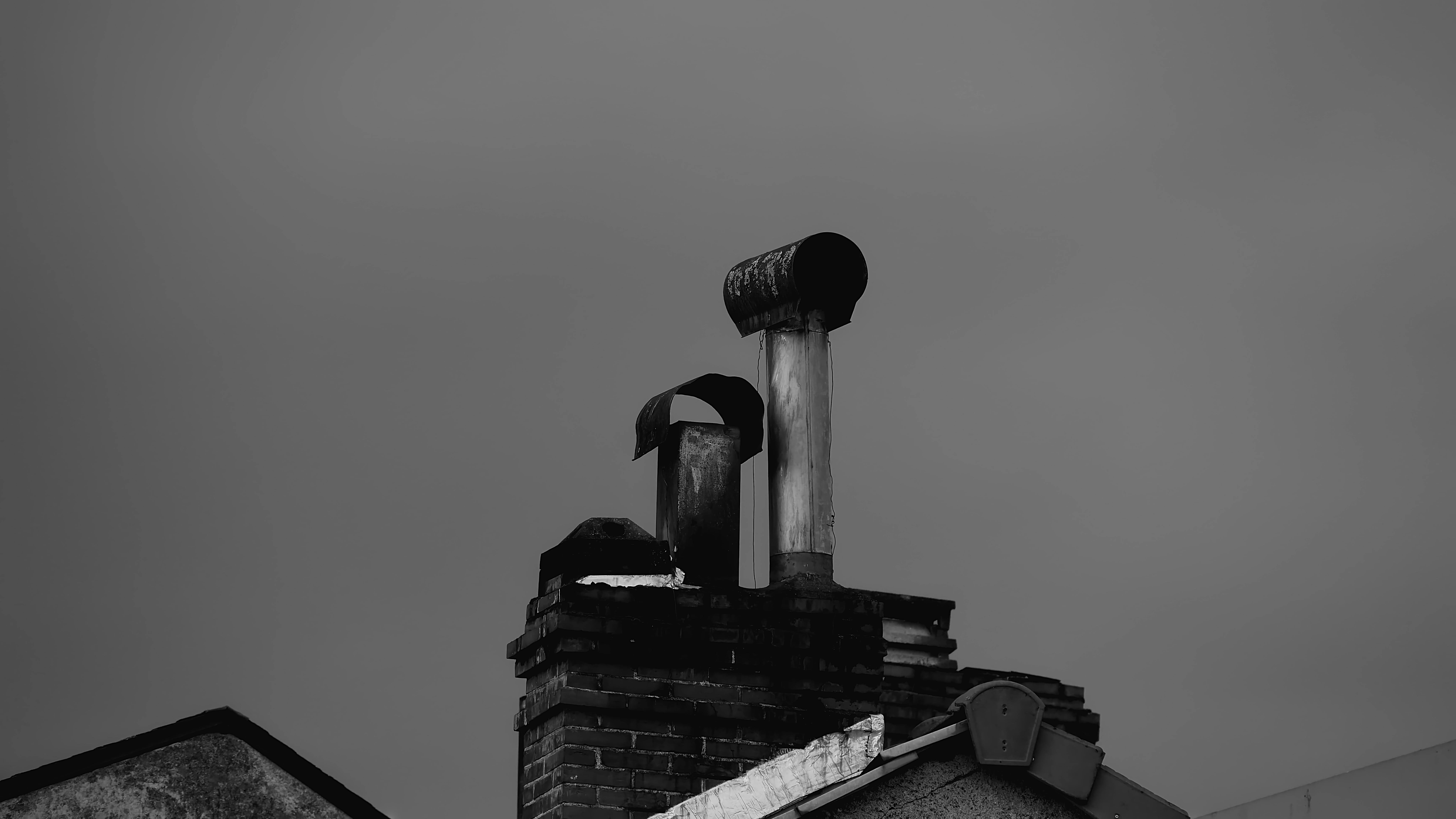 Image monochrome d'une cheminée et d'un toit rustiques, évoquant une sensation nostalgique.