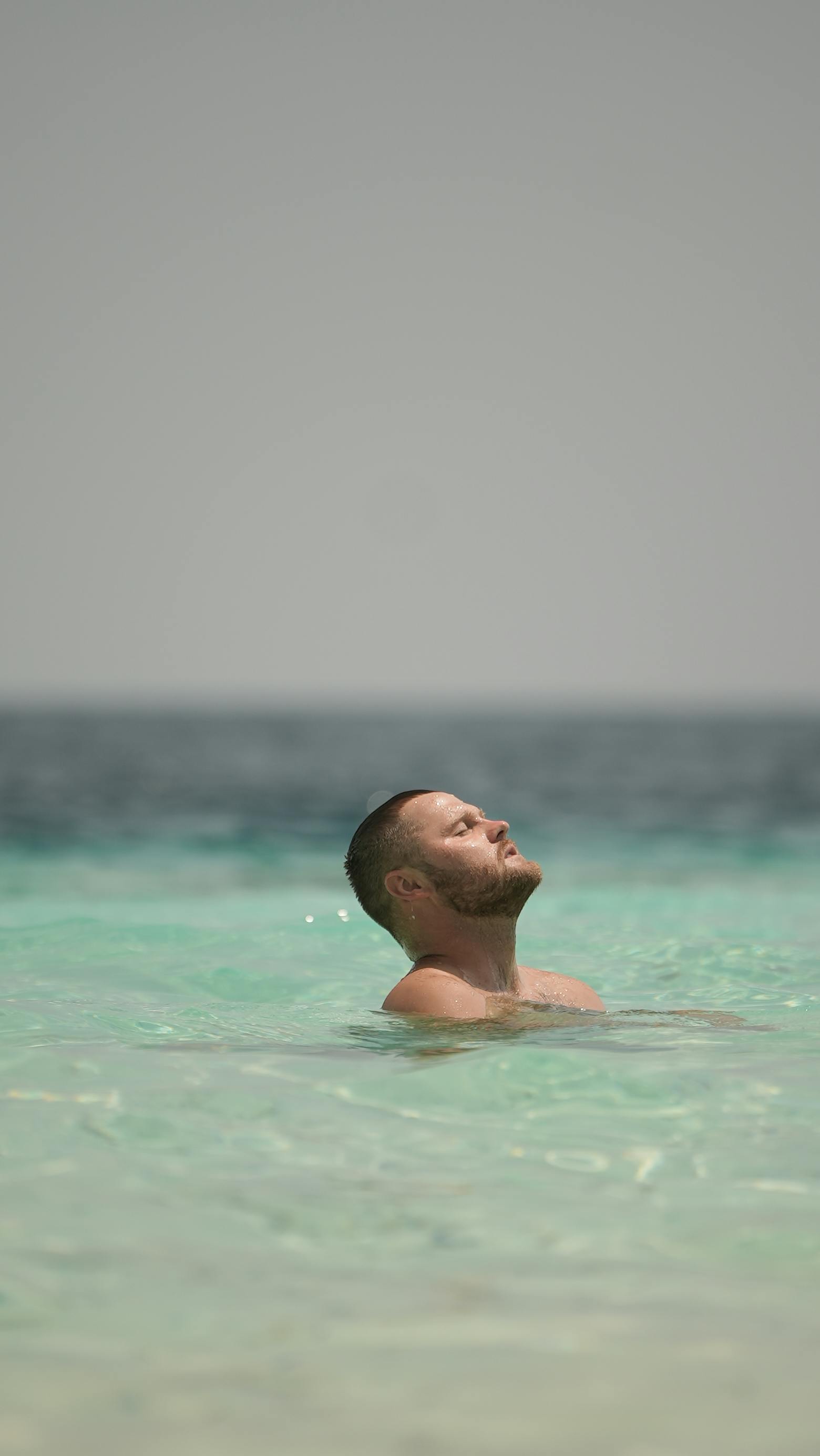 бесплатная Мужчина наслаждается спокойным днем, купаясь в бирюзовых водах Мальдив под ясным небом. Стоковое фото