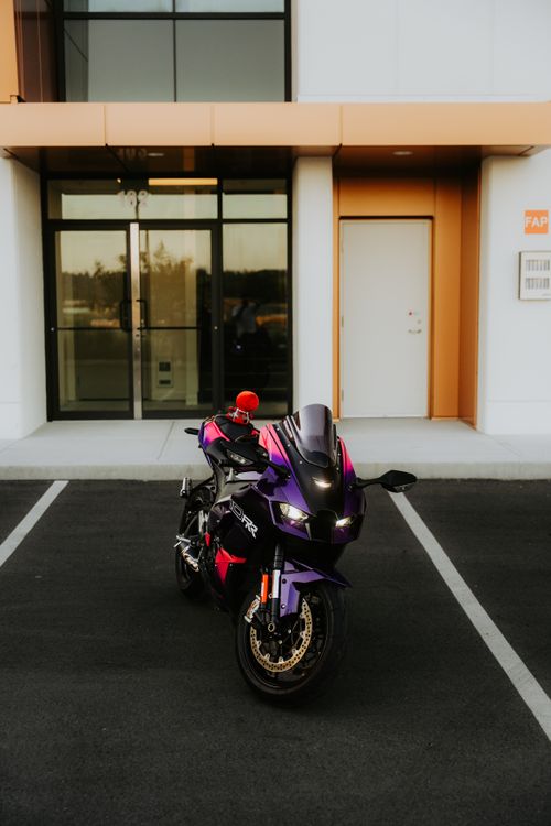 Free A vibrant purple motorcycle parked in front of a modern building, reflecting urban lifestyle. Stock Photo