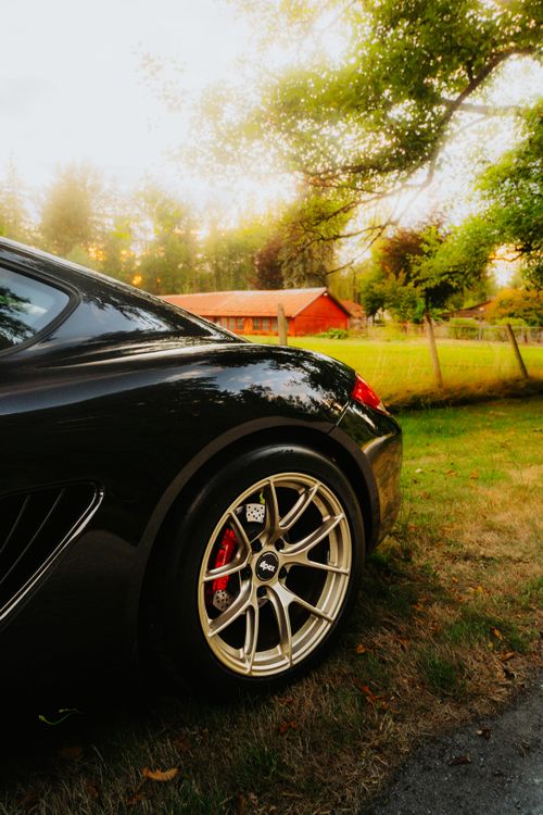 Free Stylish black car in scenic rural setting with red farmhouse at sunset, highlighting luxury and nature. Stock Photo