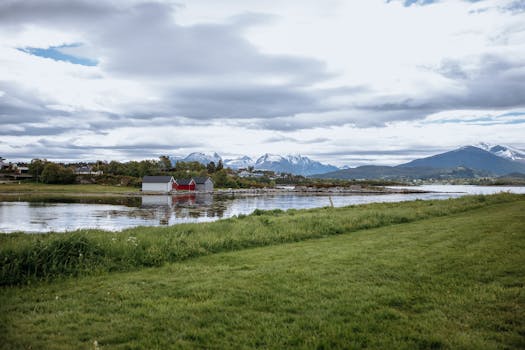 Red barn by a tranquil fjord with snow-capped mountains in Norway.