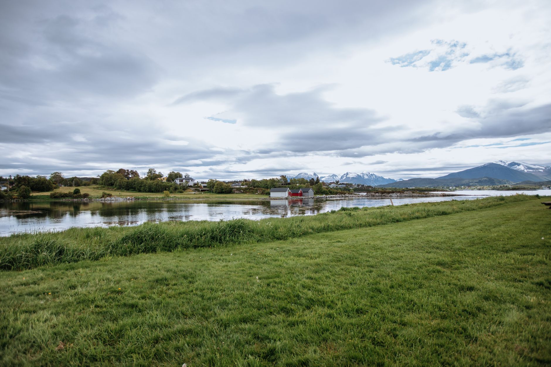 Tranquil view of a Norwegian fjord with distant mountains and lush greenery under a cloudy sky.