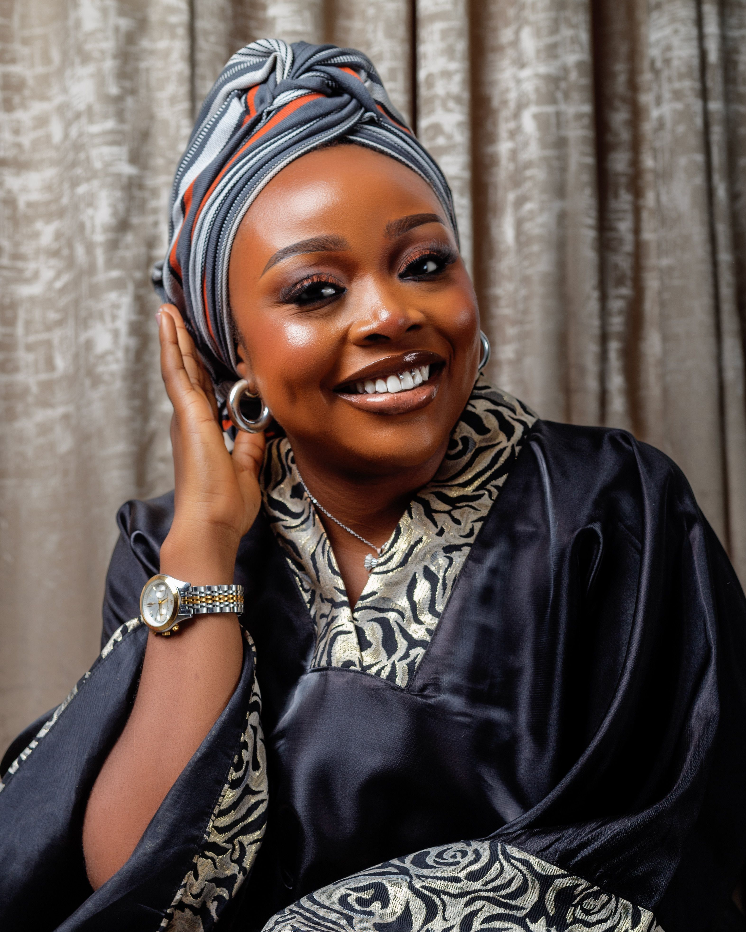 A woman in a traditional outfit and headwrap smiling confidently indoors.