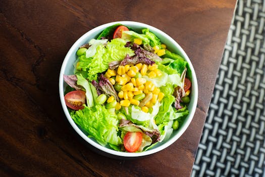 A vibrant salad with lettuce, cherry tomatoes, corn, and edamame in a white bowl.