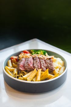 Gourmet dish of pasta with grilled steak, tomatoes, and vegetables, perfect for food photography.