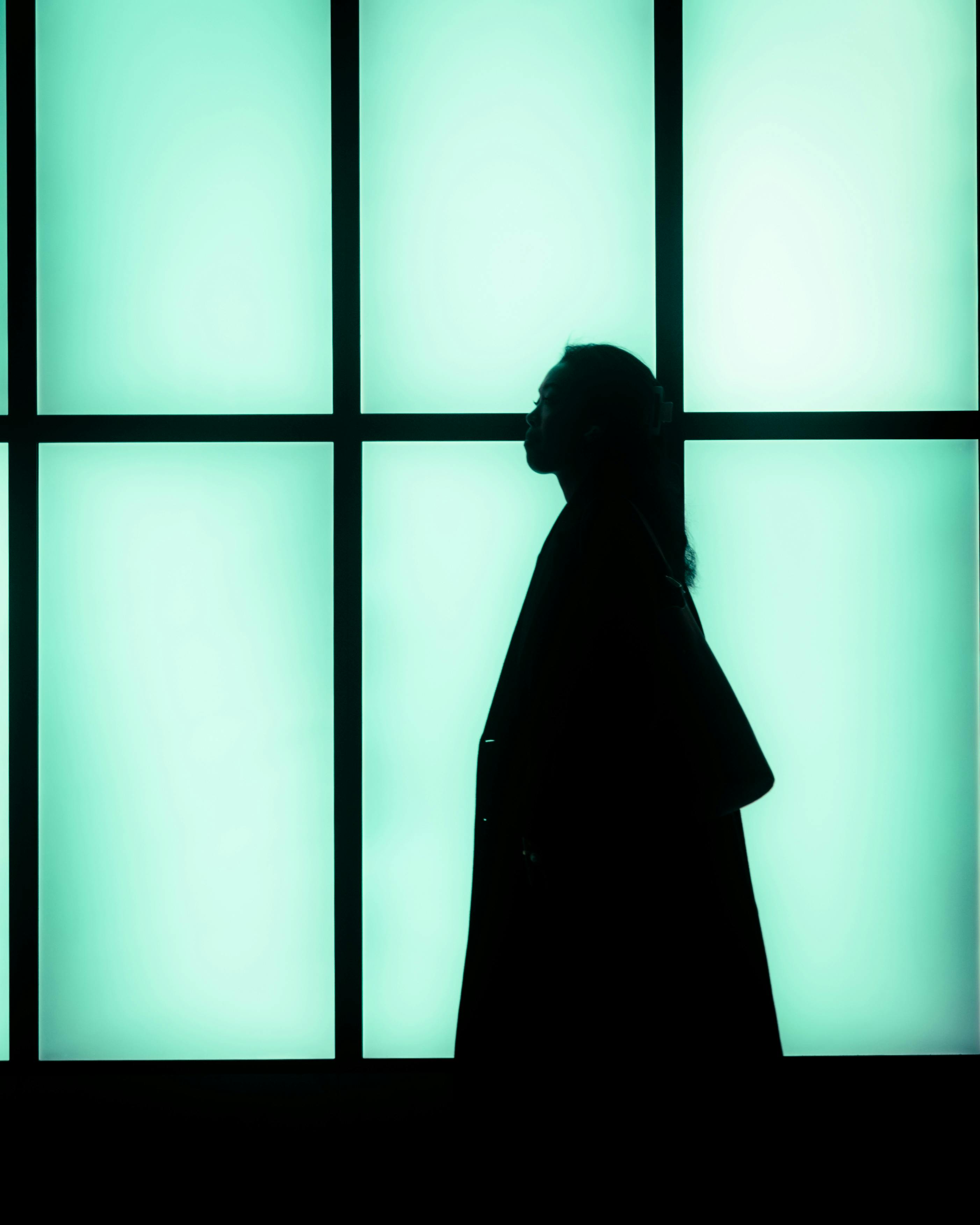 Silhouette of a woman walking past a glowing grid window in Stockholm, Sweden.