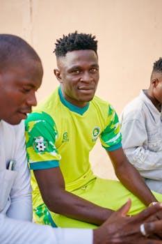 Three young men, including a soccer player in a green uniform, sitting outdoors.