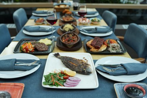 Free An elegant al fresco dining setup featuring grilled fish, side dishes, and red wine, perfect for a gourmet meal. Stock Photo