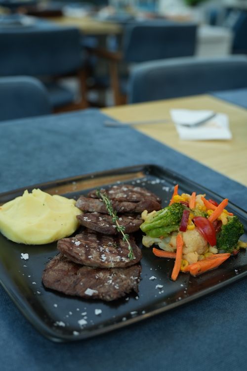 Free Savory grilled steak served with mixed vegetables and creamy mashed potatoes on a black plate. Stock Photo