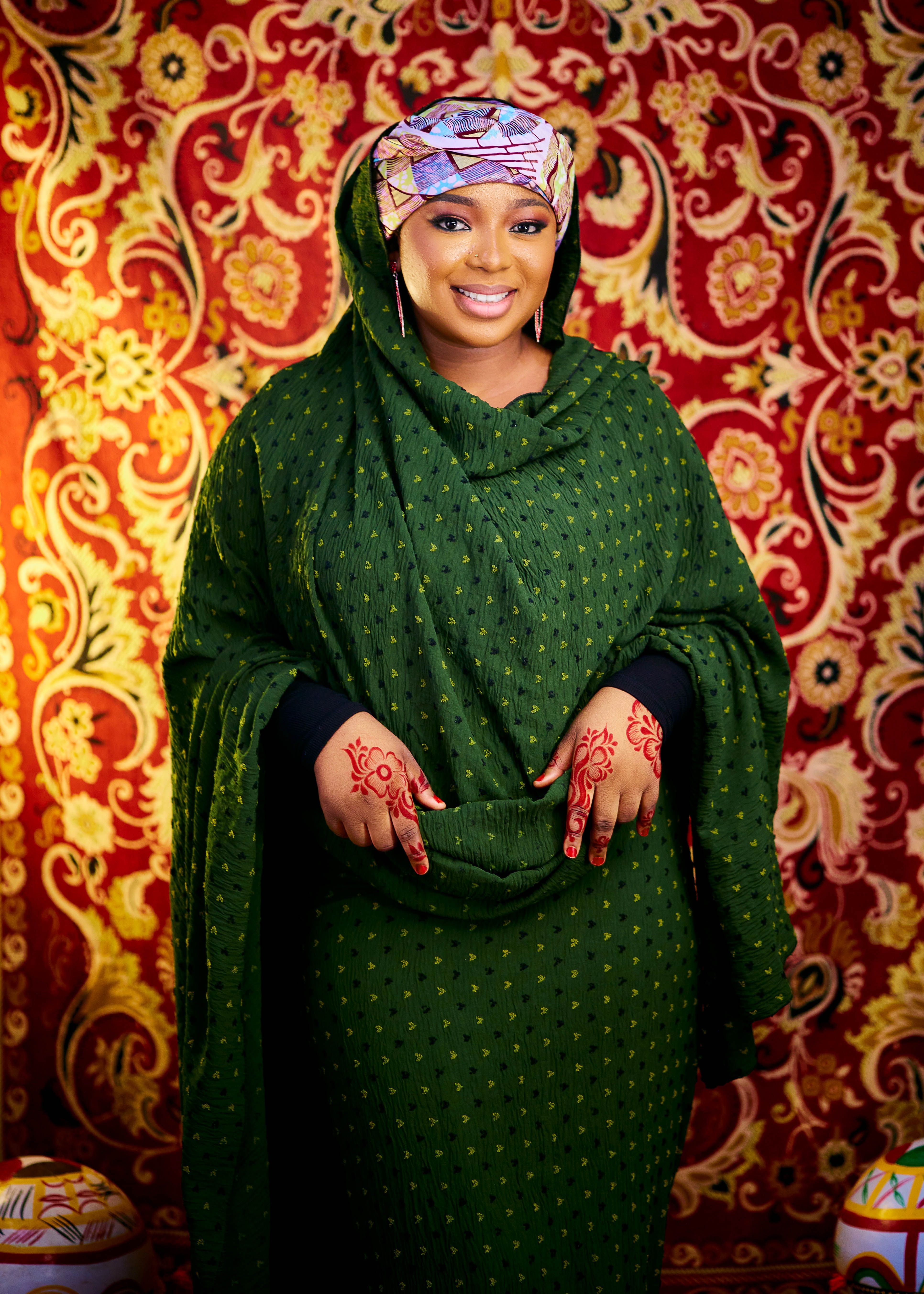 Woman in vibrant traditional clothing with henna designs, smiling against decorative backdrop.