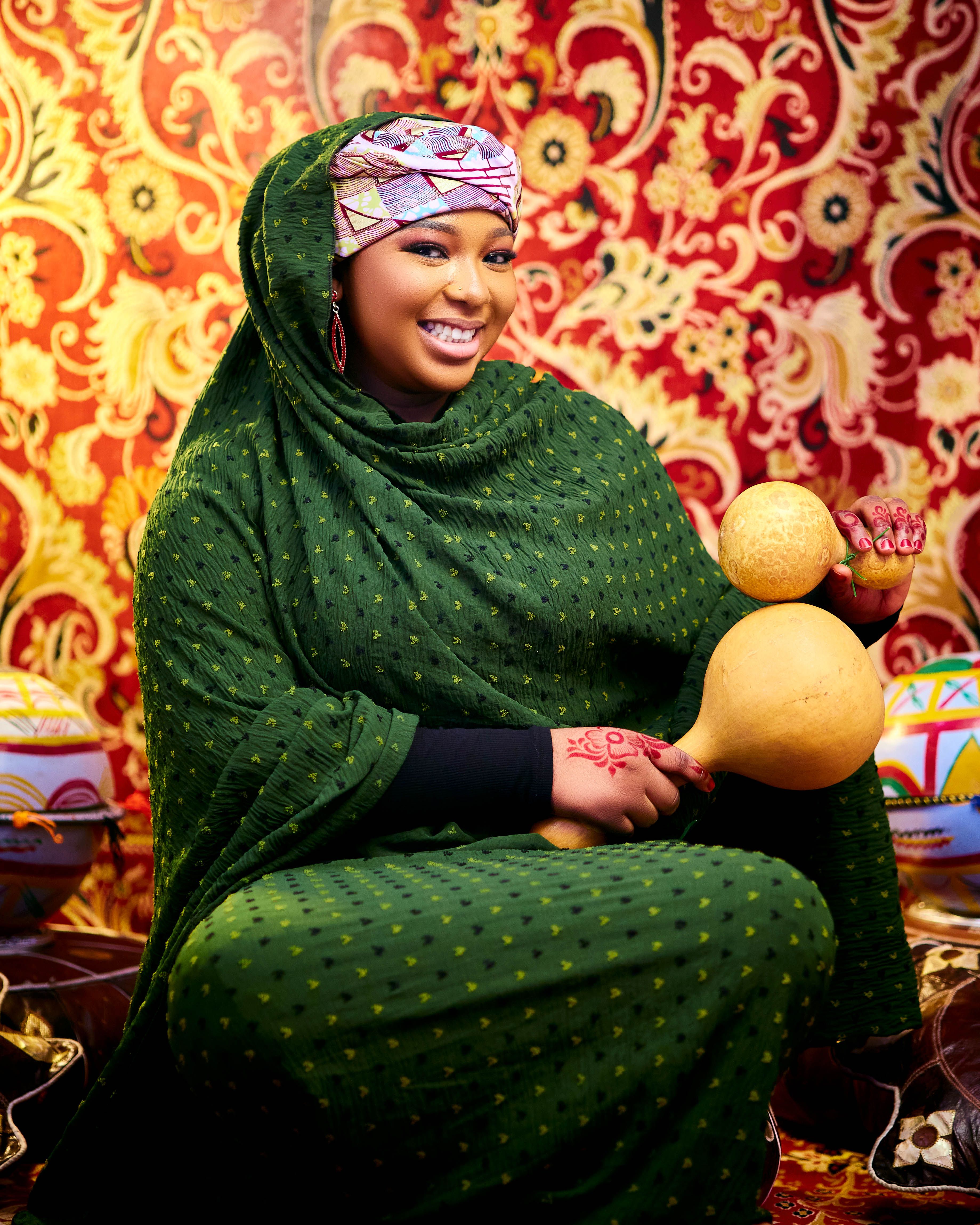 Radiant African woman wearing colorful traditional attire, holding calabash with an intricate patterned background.