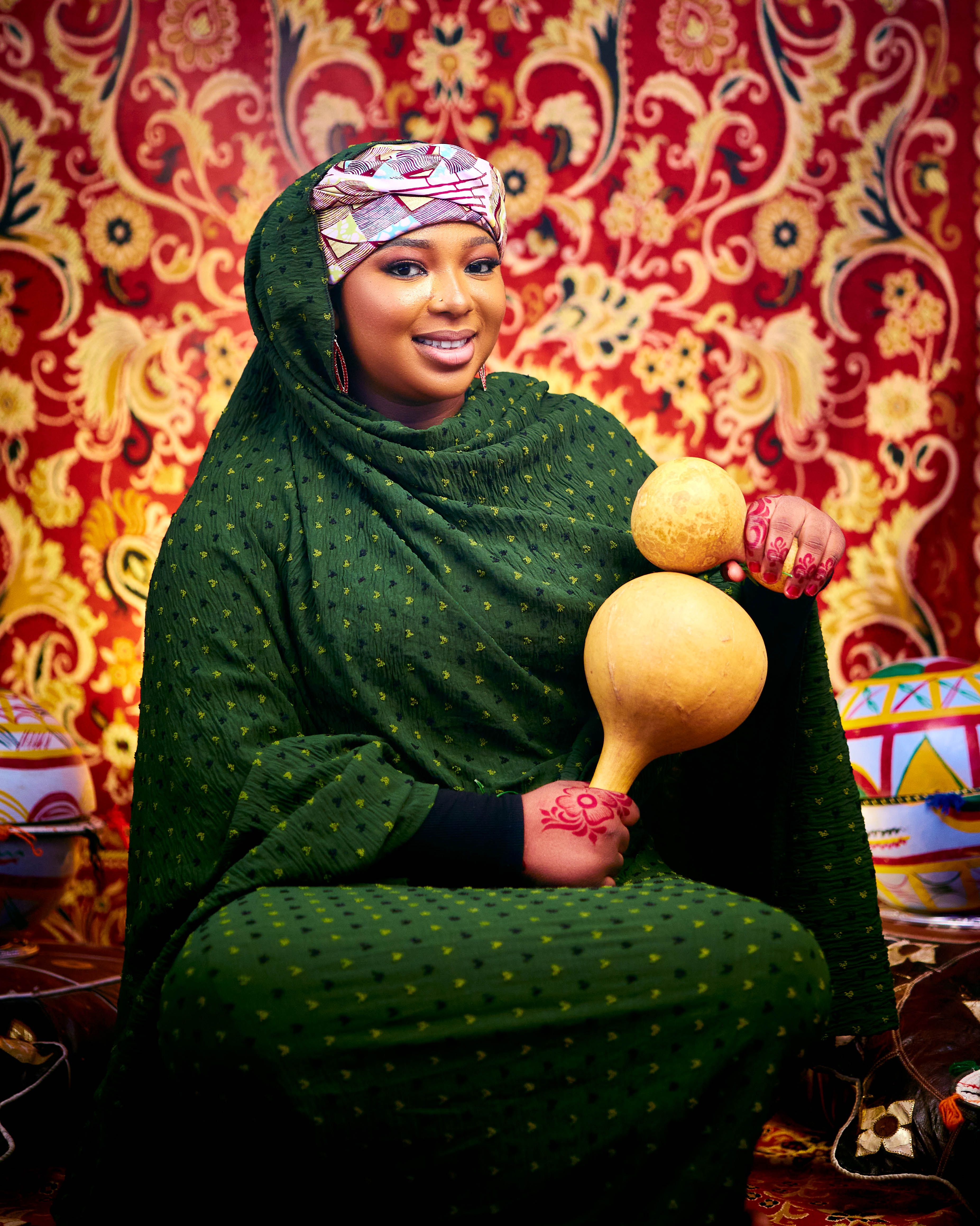 Portrait of a woman in traditional attire holding calabash with vibrant pattern background.
