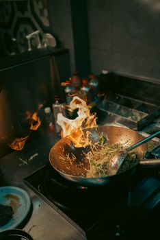 Exciting kitchen scene with stir-fried noodles in a fiery wok capturing culinary action.