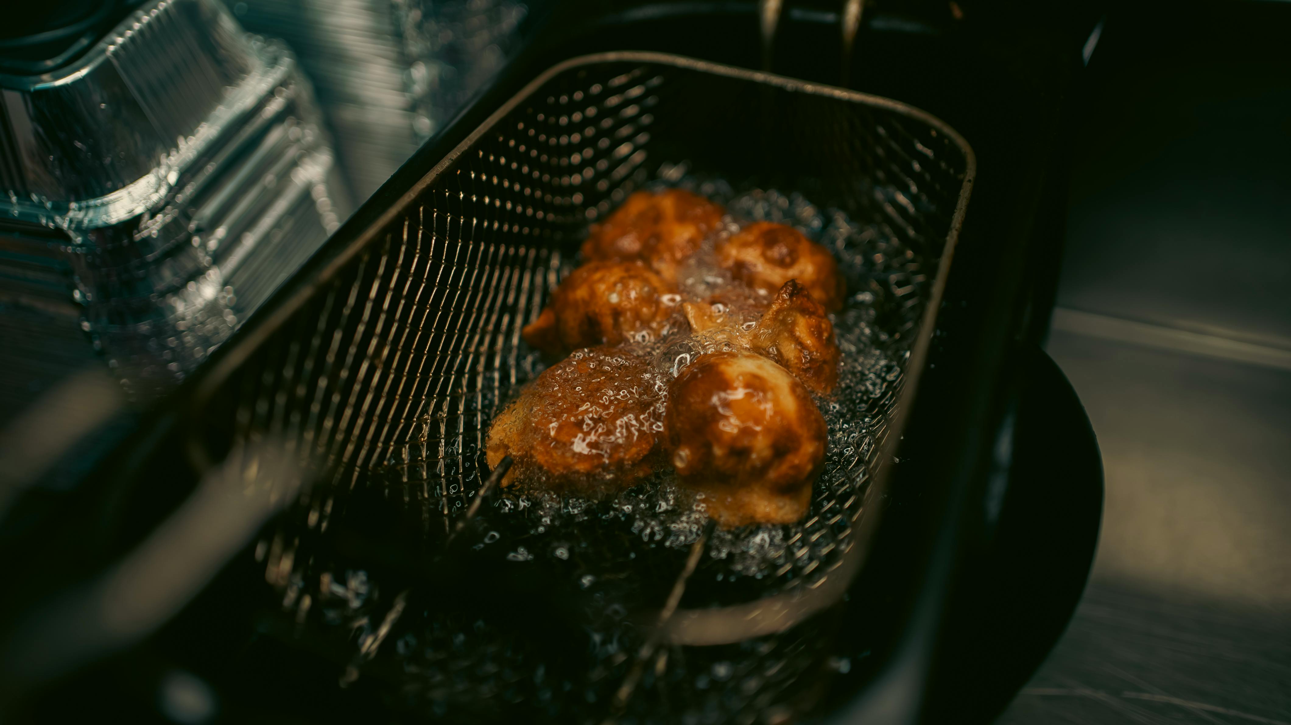 Close-up of takoyaki being deep-fried in a basket for a crispy finish.