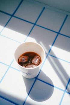 Aesthetic shot of iced coffee in a paper cup placed on blue white grid tiles.