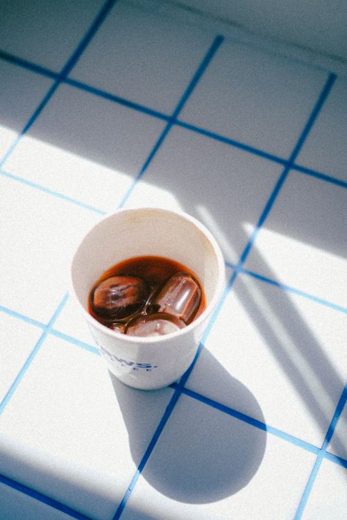 Free Aesthetic shot of iced coffee in a paper cup placed on blue white grid tiles. Stock Photo