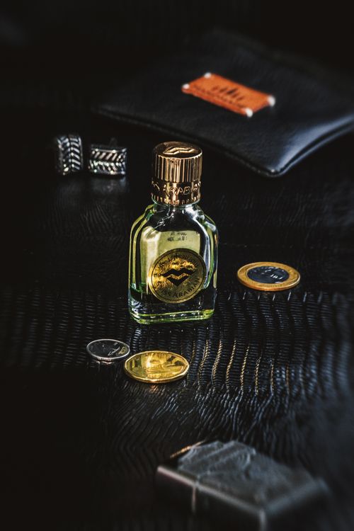 Free Elegant flat lay of a luxury perfume bottle with coins and male accessories on a black leather background. Stock Photo