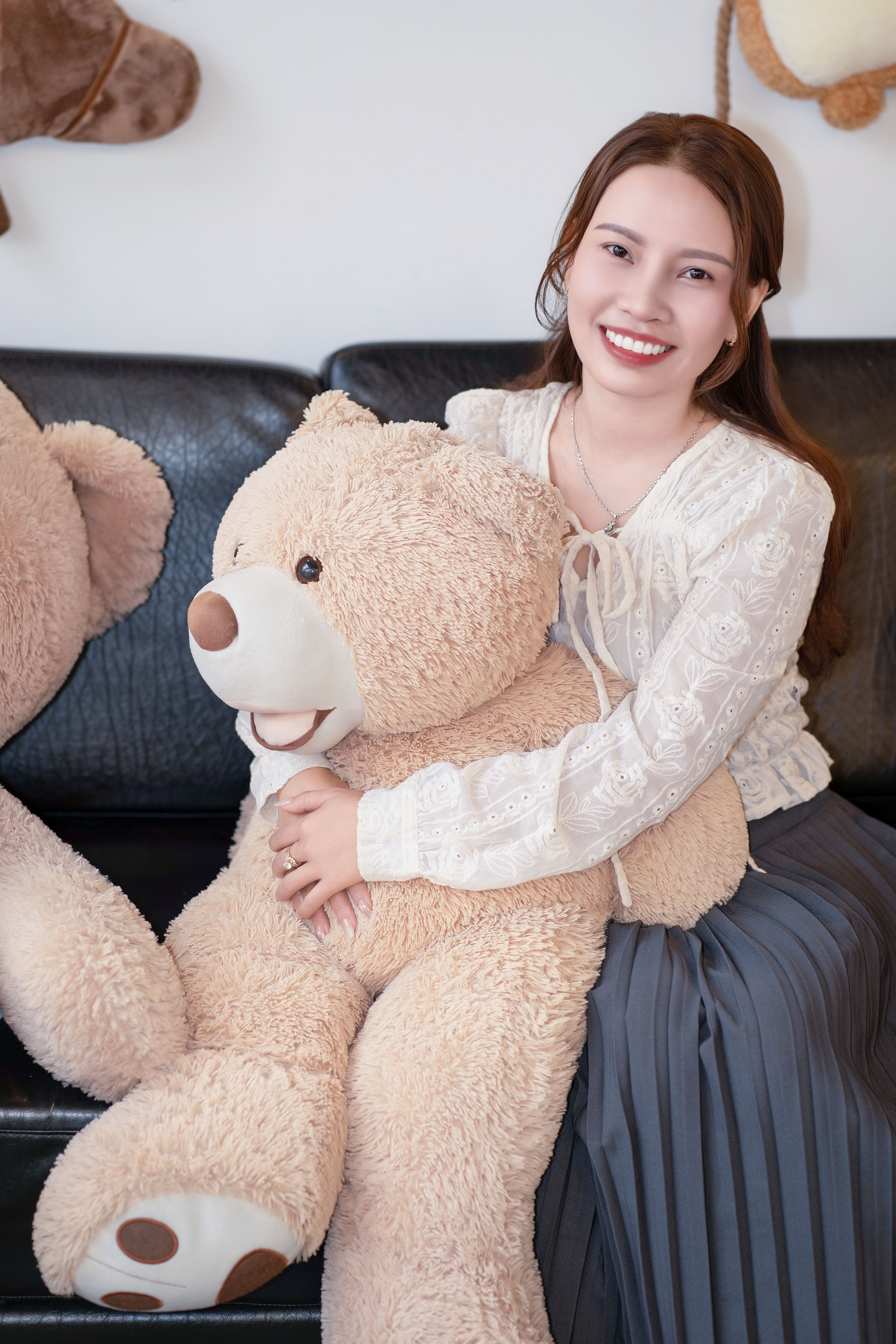 Happy woman sitting indoors hugging a large teddy bear, radiating joy and warmth.