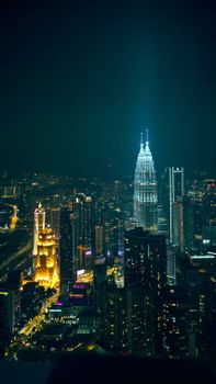 Aerial night view of Kuala Lumpur's skyline, featuring illuminated Petronas Towers.