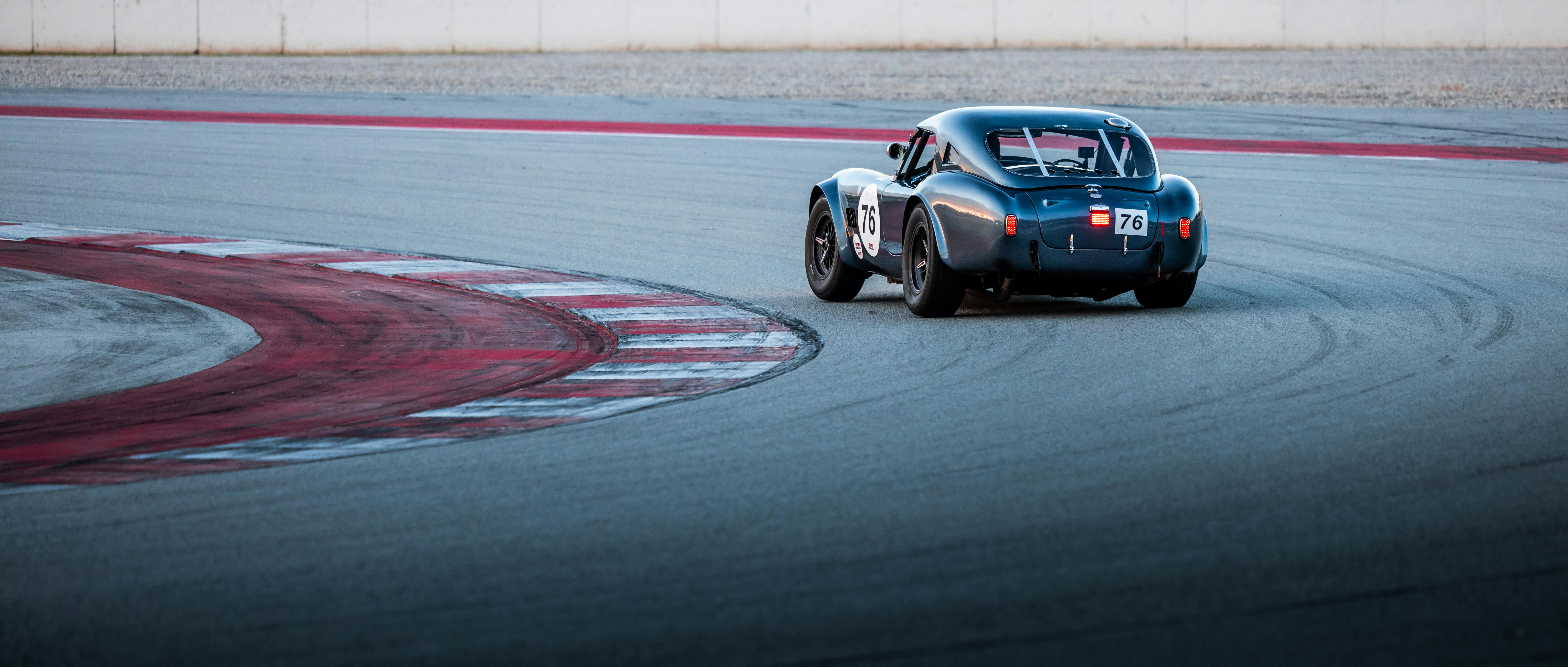 A vintage race car with number 76 navigating a sharp curve on a paved race track.