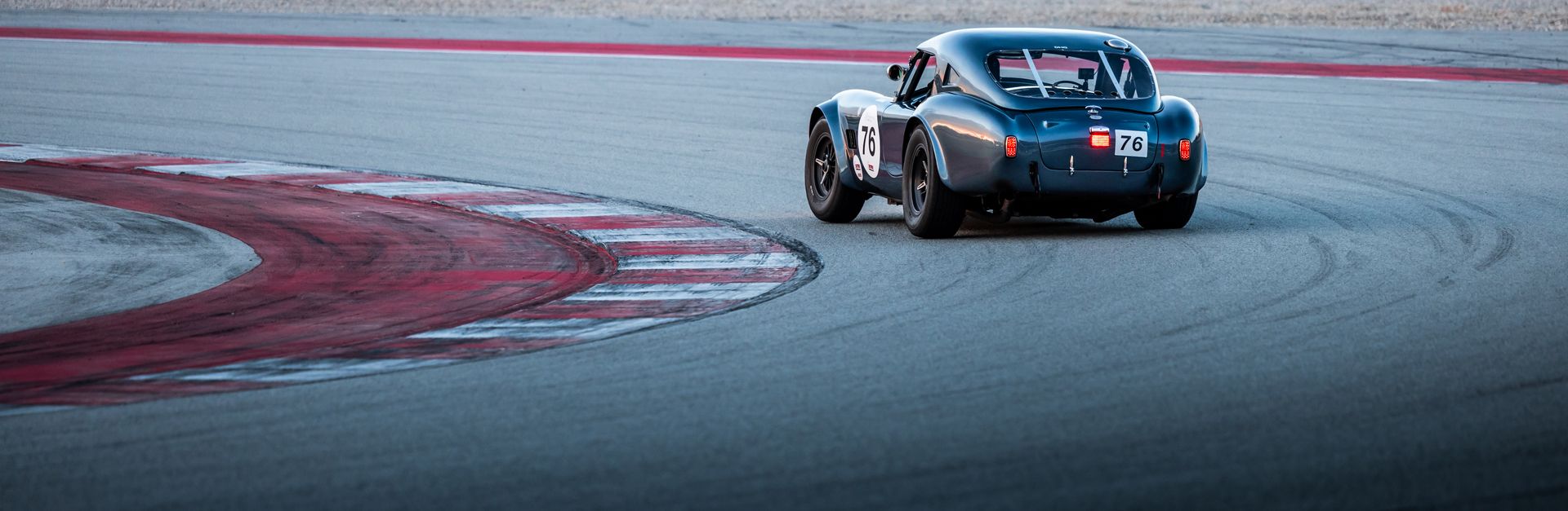 A vintage race car with number 76 navigating a sharp curve on a paved race track.