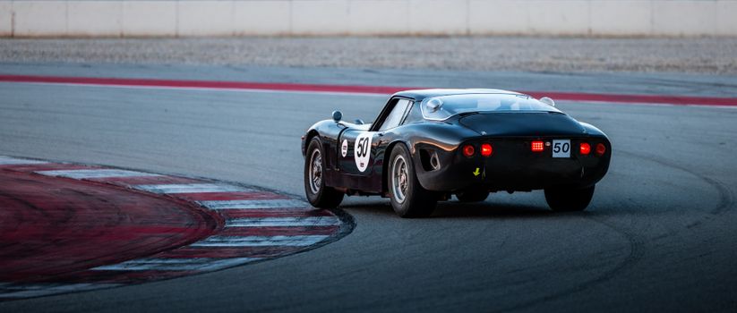 Classic black vintage race car takes a corner on an asphalt track at dusk. Speed and nostalgia in motion.