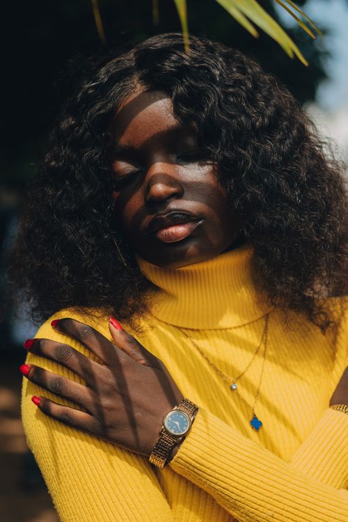 Free A woman in a bright yellow sweater with curly hair poses gracefully under natural light, highlighting her gold jewelry. Stock Photo