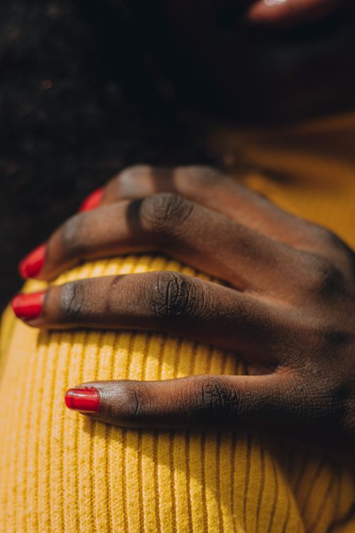 Free A close-up of a hand with red nail polish resting on a yellow sweater, showcasing contrast and texture. Stock Photo