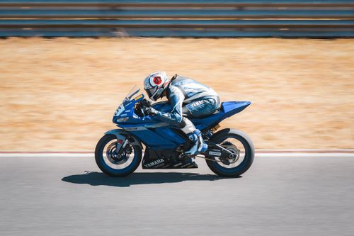Free Motorcyclist in full gear rides a blue Yamaha motorcycle on a sunny racetrack. Stock Photo
