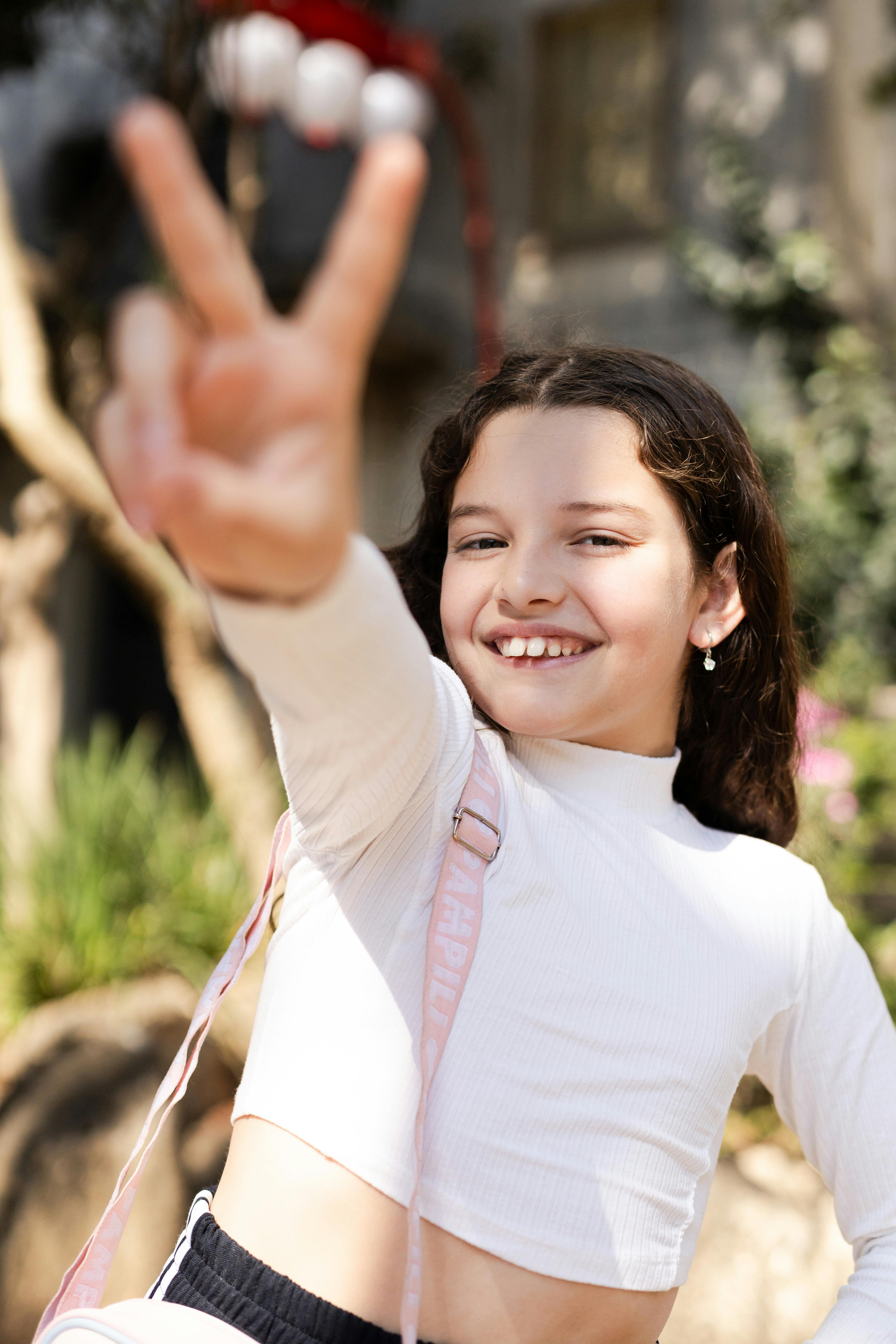 Laughing young girl making a peace sign outdoors in São Paulo, capturing youthful joy and freedom.