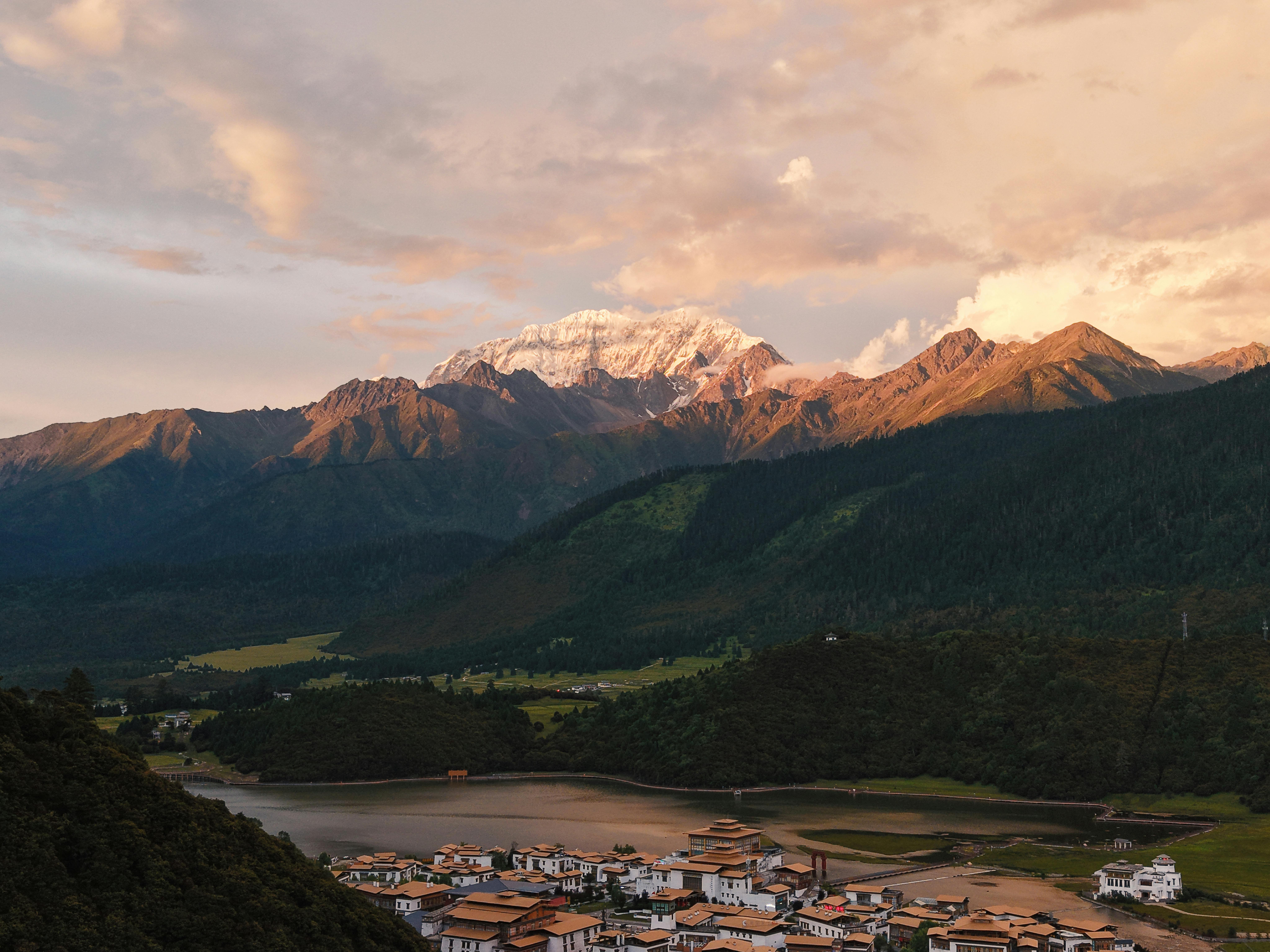 Stunning landscape of a Tibetan village nestled below snow-capped mountains at sunset.