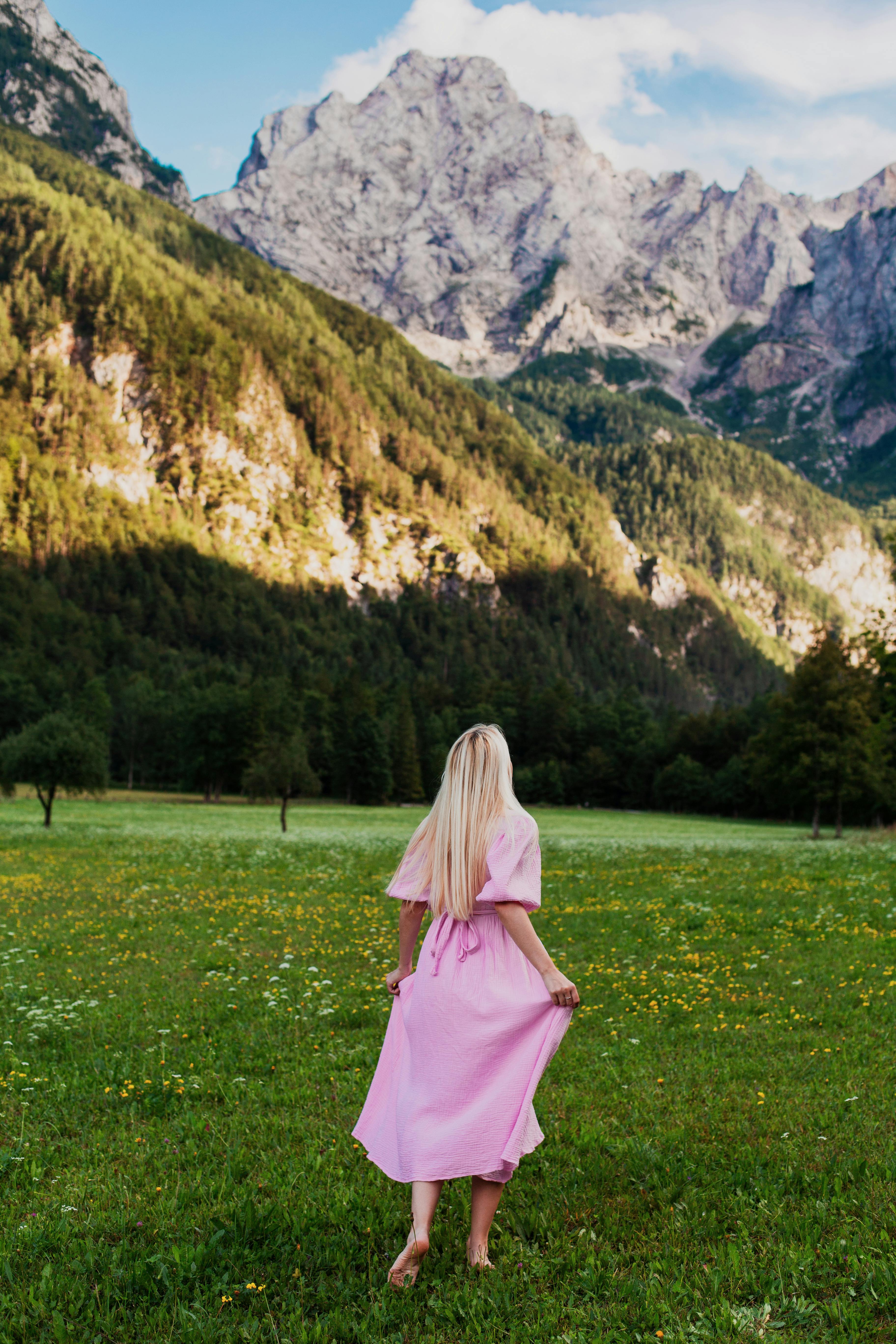 A woman in a pink dress enjoying a scenic hike in the Slovenian mountains under a bright blue sky.