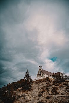A picturesque hilltop church beneath dramatic cloudy skies captures the essence of solitude and spirituality.
