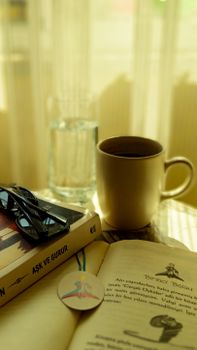 Warm indoor scene with coffee, books, and glasses for a relaxing reading session.