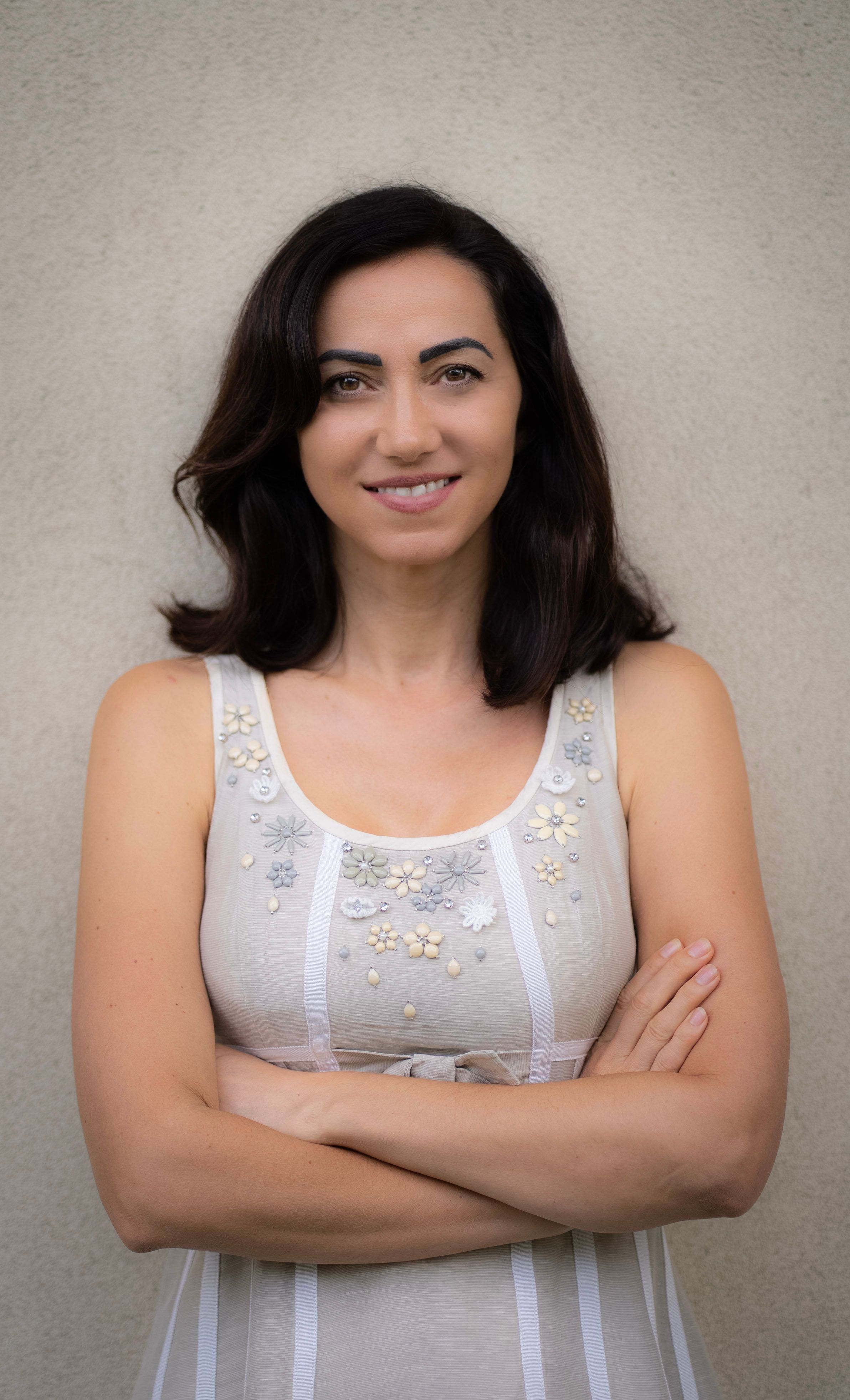 Portrait of a confident brunette woman posing with arms crossed, set against a simple backdrop in Milan, Italy.